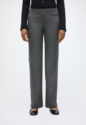 Pantalon gris droit porté avec un haut noir à manches longues et des chaussures noires à petits talons, vue de face, debout sur fond neutre.
