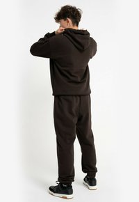 Ciemnobrązowy kaptur z pasującymi spodniami dresowymi. Miękka tkanina, luźny krój, elastyczne mankiety i sportowe buty w zestawie. Prosty design, bez wzorów.