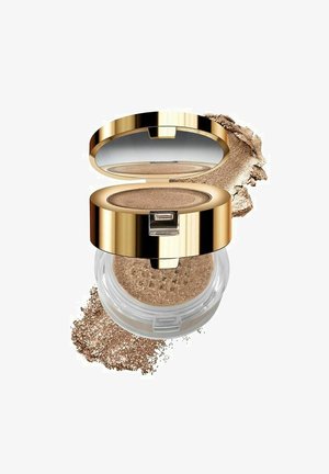 Pronssimainen vapaa puuterifoundation, joka on kirkkaassa astiassa kultaisella kannella. Hienot kimalteet näkyvät, ja hieman puuteria on ripoteltu ympäri astian pohjaa.