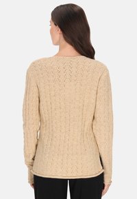 Beige kötött pulóver, textúrált, gyémánt mintával. Hosszú ujjú, kerek nyakkivágással és enyhén ívelt alsó szegéllyel. Minimalista dizájn.