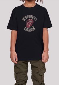 Sort bomulds t-shirt med et slidt rødt og gråt Rolling Stones tungelogo, omkranset af tekst i en fed, vintage stil.