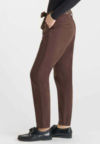 Pantaloni marroni a taper con cintura a stampa leopardata, dotati di tasche laterali e una texture liscia, abbinati a scarpe nere con lacci.