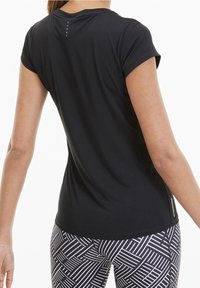 Svart atletisk t-shirt med korta ärmar, med en diskret vertikal sömdetalj på baksidan. Kombinerad med mönstrade svarta och vita leggings.