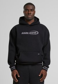 Black hooded sweatshirt with a front pocket. Features a gray "KARL KANI" logo and striped cuffs. Made of soft fabric with a relaxed fit.