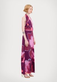 Abito halterneck in viola con grandi motivi floreali rosa, realizzato in tessuto morbido, presenta una vita aderente, gonna fluida e spacco laterale.