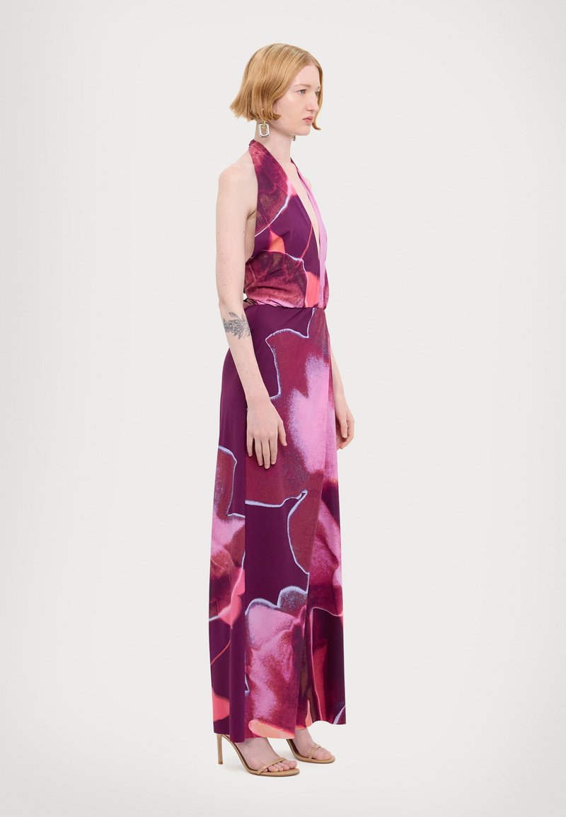 Abito halterneck in viola con grandi motivi floreali rosa, realizzato in tessuto morbido, presenta una vita aderente, gonna fluida e spacco laterale.