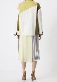Veste superposée en olive, blanc et jaune avec une coupe décontractée, associée à une jupe midi plissée en blocs de couleur dans des tons pastel.