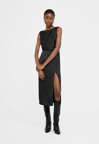 Zwart, mouwloos jurk met een zijsplit, gladde textuur, knie-lengte. Gecombineerd met glanzende zwarte kniehoge laarzen. Eenvoudig, elegant ontwerp.