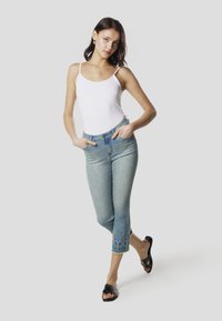 Witte nauwsluitende bodysuit, lichtblauwe cropped jeans met een geborduurd diamantpatroon langs de zoom, gedragen met zwarte slidesandalen.