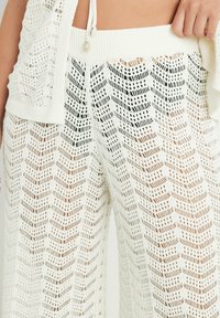 Pantalones de punto blancos de pierna ancha con un patrón de espiga y acabado texturizado. Cintura elástica con cordón de ajuste y detalles en perlas.