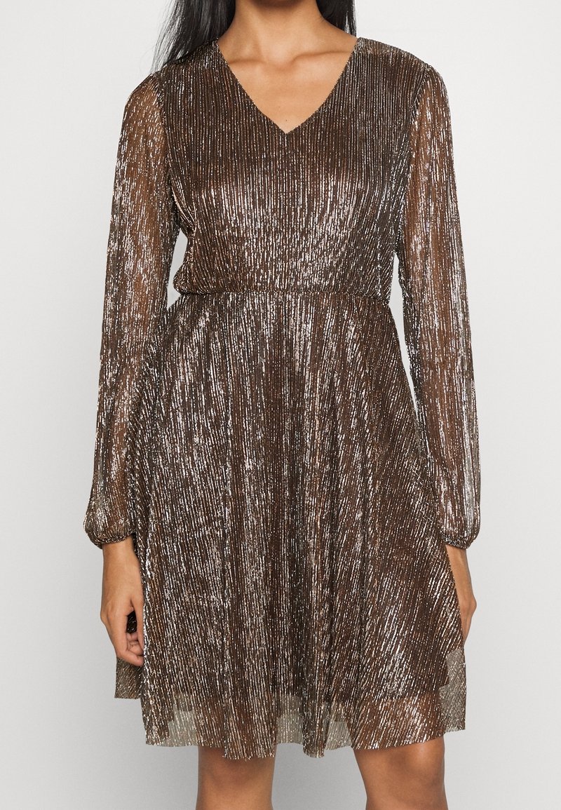 Femme portant une robe marron scintillante, longueur genou, manches longues, plis verticaux et encolure en V.