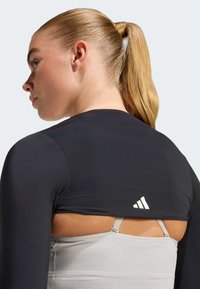 Czarny sportowy top z długimi rękawami, krótki fason, z szarą warstwą pod spodem. Charakterystyczne białe logo Adidas na plecach.