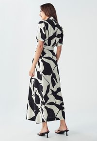 Čierno-biela dlhá šaty s listovým vzorom, krátkymi rukávmi, priliehavým pásom a splývavou sukňou. Textúrovaná látka s gombíkovým golierom.