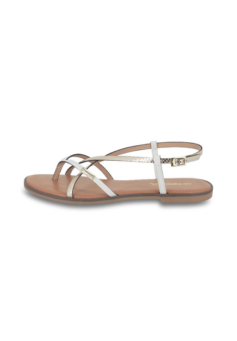 Platte sandalen met een lichtbruine zool, witte en metallic banden en een gespsluiting. De banden hebben een kruisontwerp voor een minimalistische uitstraling.