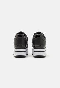 Chaussures à plateforme noires avec une texture brillante, des rayures blanches et des détails arrière prononcés. Talon arrondi avec une silhouette courbée.