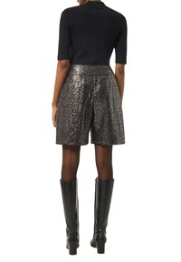 Czarny dzianinowy top z krótkimi rękawami połączony z wysokimi na biodrach, metaliczno-srebrnymi szortami z brokatem. Modelka nosi czarne kozaki na wysokim obcasie do kolan.