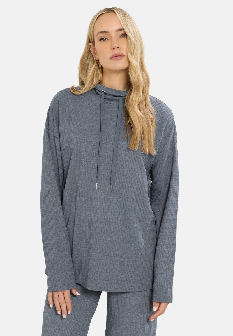 Harmaa ribattua pitkähihaista paitaa, jossa on korkea kaulus, pujotusnyörit ja rento istuvuus. Pehmeä kangas, jossa on struktuurikuosi, yhdistettynä vastaaviin housuihin.