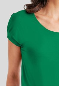Groene T-shirt met korte mouwen en een ronde hals. De stof lijkt glad en lichtgewicht, met subtiele stikdetails langs de randen.