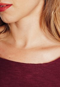 Top bordeaux senza spalle con una texture liscia, caratterizzato da un ampio scollo e cuciture sottili lungo il bordo, abbinato a toni neutri della pelle.