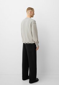 Hellgrau gestrickter Pullover mit Rippenbund und ausgefransten Akzenten, kombiniert mit lockeren schwarzen Hosen. Einfaches, entspanntes Design und Materialien.