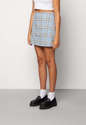 Jupe mini à carreaux bleus avec une coupe ajustée, associée à un crop top blanc, portée avec des mocassins noirs épais et des chaussettes blanches.