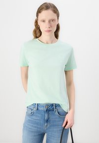 Lys grønn bomull t-skjorte med korte ermer, rund hals og diskret brodert logo på venstre bryst. Kombinert med blå jeans.