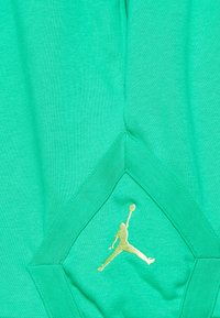 Zelená džersejová tkanina s zlatým logem Jumpman. Design zahrnuje akcent v tvaru diamantu na lemu s kontrastním detailem.