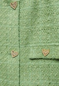Tissu vert texturé avec trois boutons dorés en forme de cœur décorés de petits cristaux.