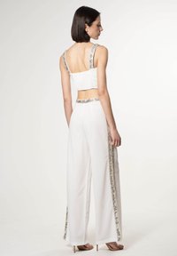 Top corto blanco con tejido texturizado y tirantes con acentos plateados, combinado con pantalones anchos blancos con detalles plateados en los lados.