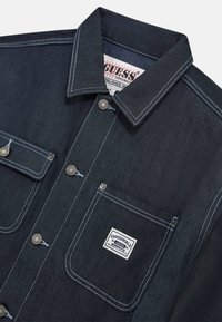 Denimoverhemd in donkerblauw met contrasterende witte stiksels. Bevat een gekraagde kraag, drukknoopsluitingen en twee borstzakken met een label.