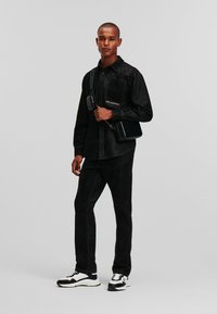 Cămașă din denim negru cu guler cu nasturi, pantaloni din denim negru și o geantă crossbody neagră. Adidași albi și negri cu sireturi.