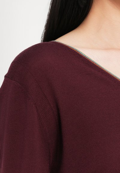 Burgunderfarbener Strickoberteil mit weitem Ausschnitt, einem mehrfarbigen Akzentstich und kurzen Ärmeln, der eine strukturierte Oberfläche zeigt.