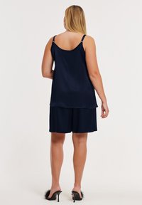 Marineblaues Satin-Schlafset mit locker geschnittenem Top mit verstellbaren Trägern und passenden Shorts. Inklusive schwarzer, flauschiger Hausschuhe mit Absatz.