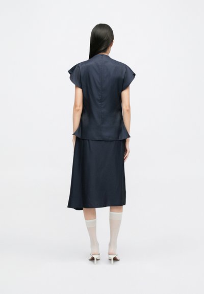 Navy peplum dress with short flutter sleeves, smooth fabric, knee-length skirt, and discreet back zipper. Paired with white knee-high socks.