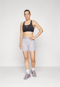 Svart sportsbh med hvit logo, grå tettsittende shorts, hvite sokker og grå joggesko. Glatt stoff og lett design.