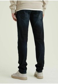 Jeans in denim blu scuro con vestibilità dritta, dotati di tasche posteriori e con una leggera scoloritura. Abbinati a sneakers chiare e a una felpa beige.
