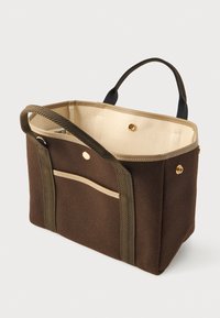 Καφέ τσάντα tote με μπεζ εσωτερικό, δύο ανθεκτικές λαβές, εξωτερική τσέπη και χρυσές κουμπωτές κλείσεις σε απλό φόντο.