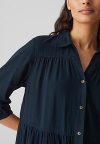 Abito button-up in un blu navy scuro con colletto, vita arricciata e maniche a sbuffo tre quarti, realizzato in tessuto morbido.