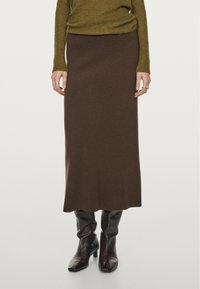Brauner Wollschnitag mit taillierter Taille und ausgestellt geschnittenem Saum, kombiniert mit schwarzen, spitzen Kniebots. Strukturiertes Strickoberteil ist teilweise sichtbar.
