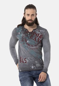 Graues Langarmshirt mit verschiedenen Texturen und Drucken, mit roten und türkisfarbenen Grafiken, einem V-Ausschnitt und dezenten Rippdetails.