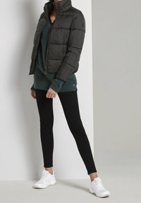 Doudoune noire à col montant, associée à un pull en tricot teal, un jean skinny noir et des chaussures de sport blanches.