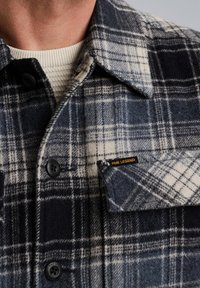 Ruudullinen flanellipaita tummansinisessä ja kermassa, jossa on nappisulku, terävä kaulus ja rintatasku, jossa on keltainen PME LEGEND -merkki.