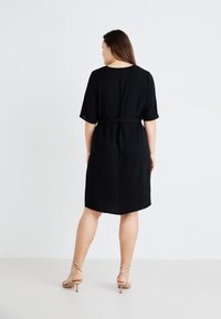 Black linen dress with a relaxed fit, short sleeves, and a tied waist. Plain design with a subtle sheen and knee-length hem.