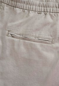 Material bej cu talie elastică și o buzunar spate orizontal, tip fanta, cu cusături vizibile.