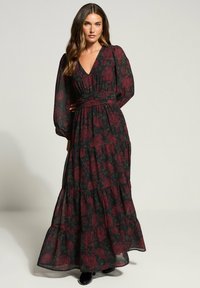 Robe maxi florale en tissu noir transparent, ornée de motifs de roses rouges et vertes, avec de longues manches bouffantes, une taille cintrée et une jupe à volants.