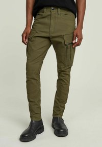 Pantaloni cargo verde oliva con multiple tasche, dettaglio con zip sul lato, vestibilità affusolata, materiale in cotone e cuciture a contrasto.