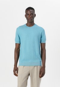 Pulover s kratkimi rokavi, svetlo modre barve, s teksturno vzorcem, okroglim izrezom in rebrastimi manšetami ter robom, v kombinaciji s svetlo bež hlačami.