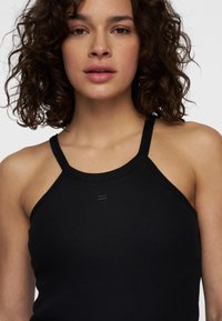 Zwarte geribde tanktop met een hoge halslijn en smalle bandjes, met subtiele branding aan de voorkant. Zachte stof met een aansluitend ontwerp.