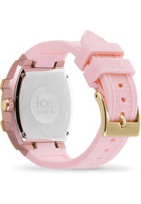 Montre de sport avec un bracelet en silicone rose, un cadran en métal rose doré, un dos en acier inoxydable et des détails texturés sur le bracelet. Fermeture à boucle dorée.