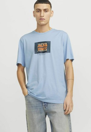 Světle modré tričko s krátkým rukávem, na kterém je čtvercové logo s nápisem "JACK&JONES" v oranžové barvě na tmavém pozadí a uvolněným střihem.